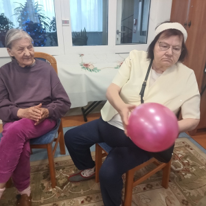 Dwie Seniorki siedzące na krzesłach. Jedna z balonem w dłoniach.