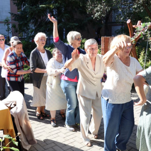 Grupa Seniorów tańcząca w ogrodzie.