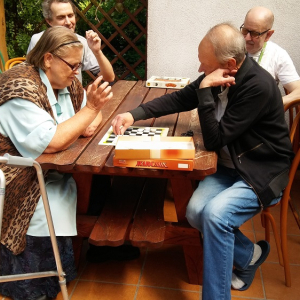 Seniorzy przy stolikach na tarasie grający w warcaby