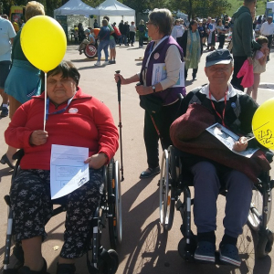 Dwoje Seniorów z DPS CHEMIK z żółtymi balonami, na tle tłumu w Parku